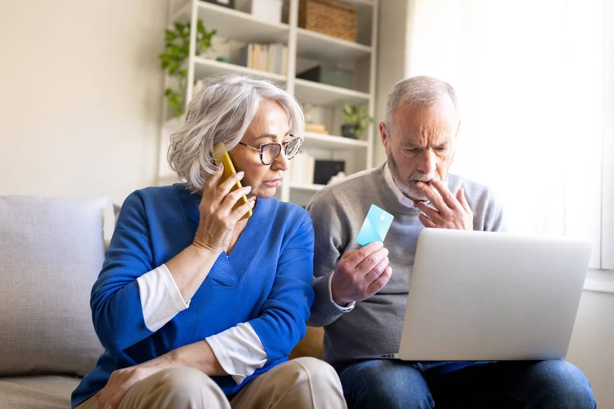 Mains d'une personne inquiète tenant un smartphone au-dessus d'une table avec des enveloppes ouvertes, lumière dramatique latérale, pas de texte lisible à l'écran